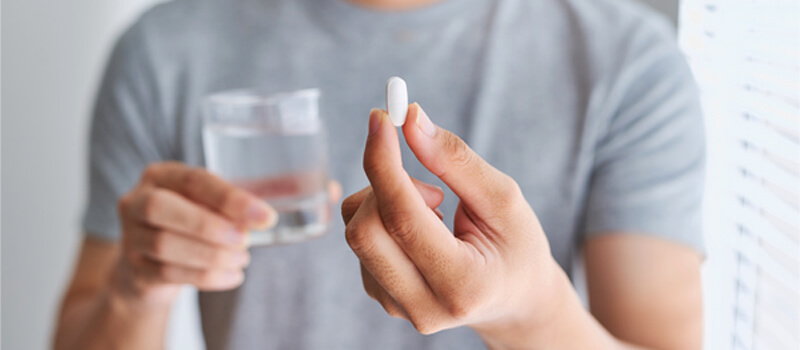 A man holds a Ginglitz Plus capsule in one hand and a glass of water in the other, preparing to take the supplement.