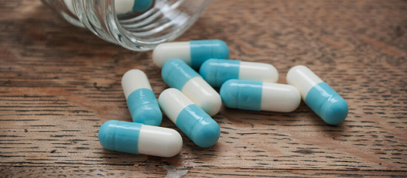 A collection of blue and white pills scattered on a wooden table surface, showcasing their distinct colors and shapes.