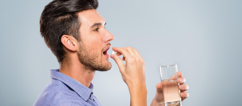 A man takes a Gluta White capsule while drinking water, highlighting the benefits of this supplement for skin health.