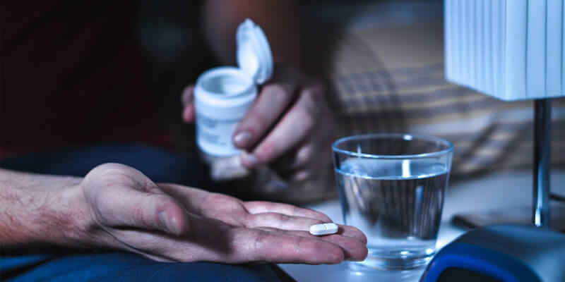A man prepares to take a pill with a glass of water, illustrating the use of herbal supplements like Ginkgo Biloba.