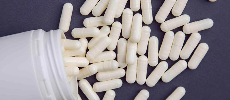 A white container tipped over, releasing white pills, symbolizing the proper intake of Gluta White capsules.