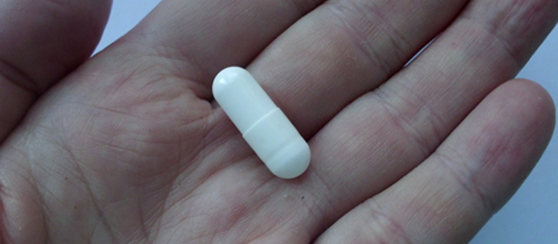 A person's hand holding a white pill, symbolizing the growing trend of Gluta White capsules in Pakistan.