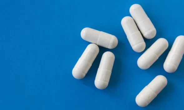 White Gluta White capsules arranged on a blue surface, promoting fast whitening benefits for skin enhancement.